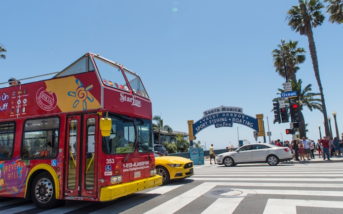 Red double-decker tour bus near Santa Monica Pier entrance, Los Angeles.
