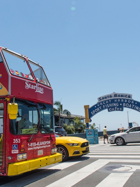 Red double-decker tour bus near Santa Monica Pier entrance, Los Angeles.