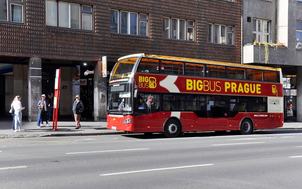 People waiting at a bus stop for the Big Bus Hop on Hop Off tour in Prague.