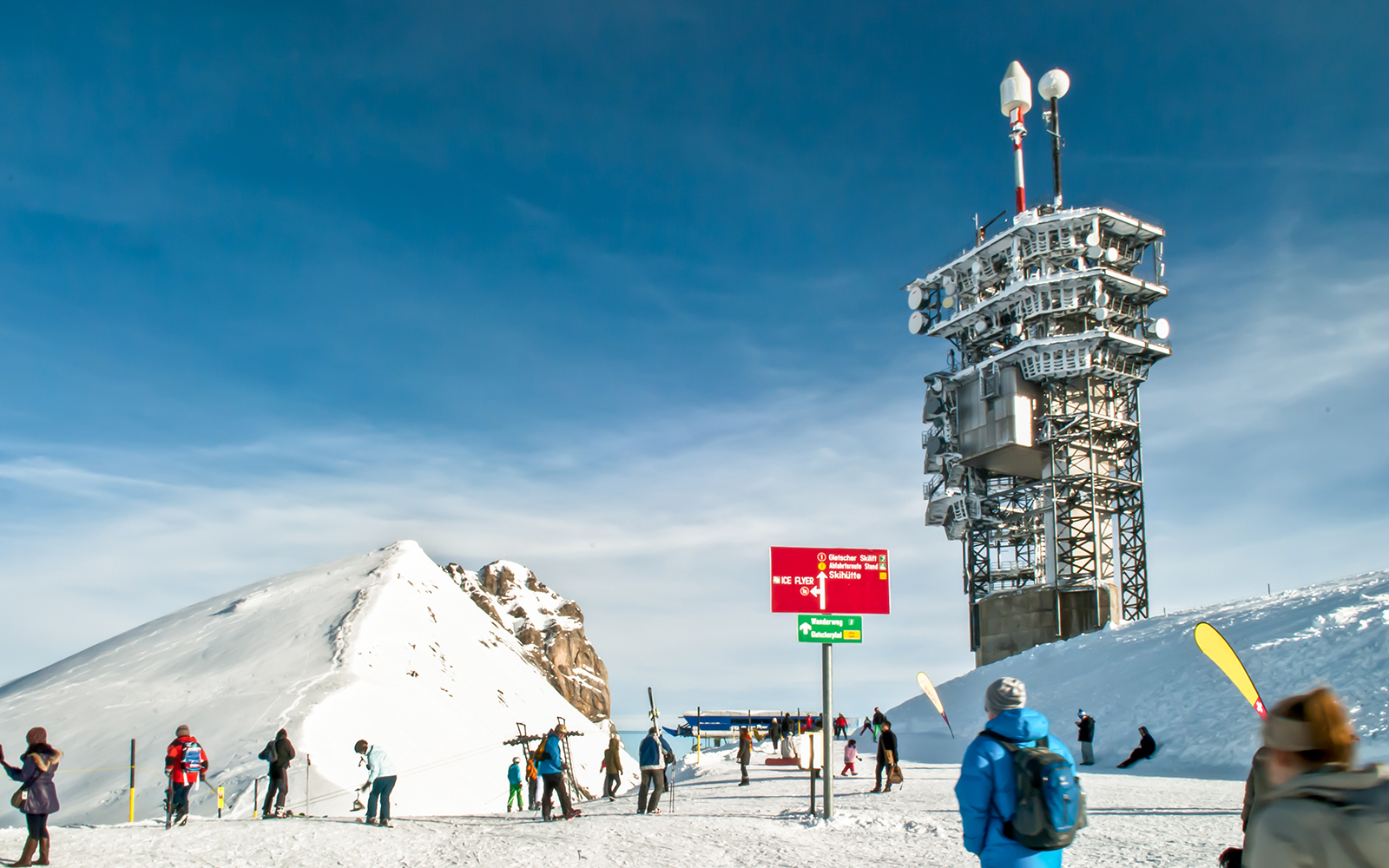 Tourists at Mount Titlis summit with snowy landscape and observation tower.