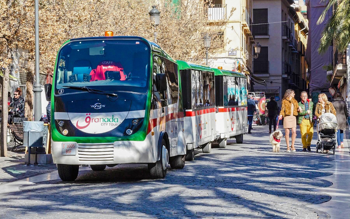 Granada city tour bus on a street with people walking nearby.