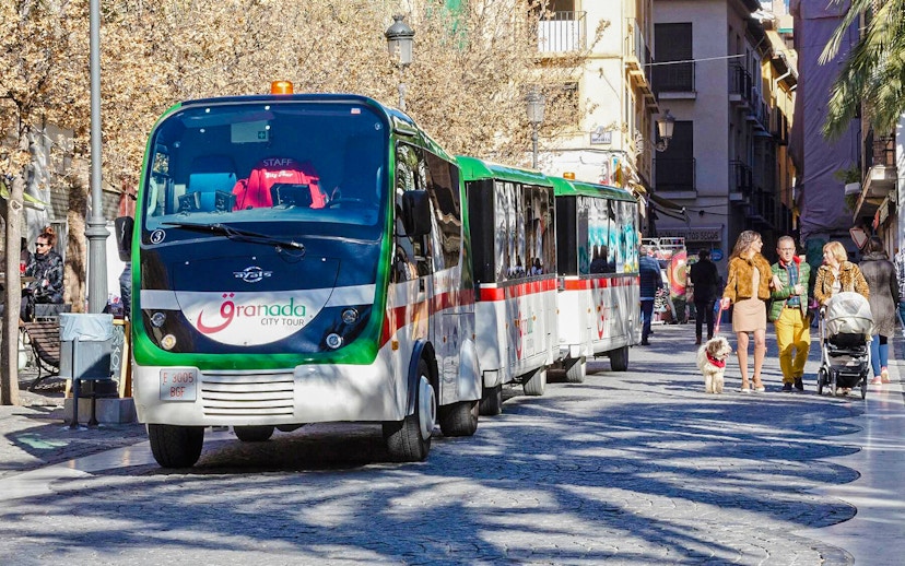 Granada city tour bus on a street with people walking nearby.