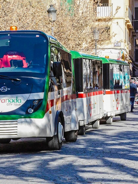 Granada city tour bus on a street with people walking nearby.