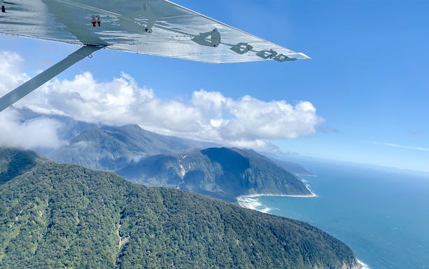 Aerial view of Tasman Sea coastline and lush mountains from aircraft.