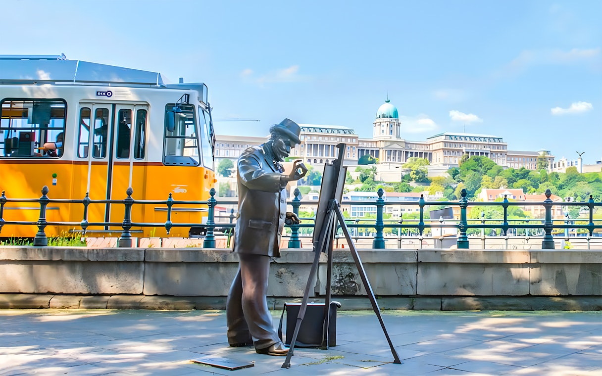 Tram passing by a statue of a painter with Buda Castle in the background, Budapest.