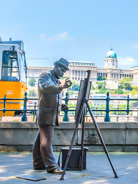 Tram passing by a statue of a painter with Buda Castle in the background, Budapest.