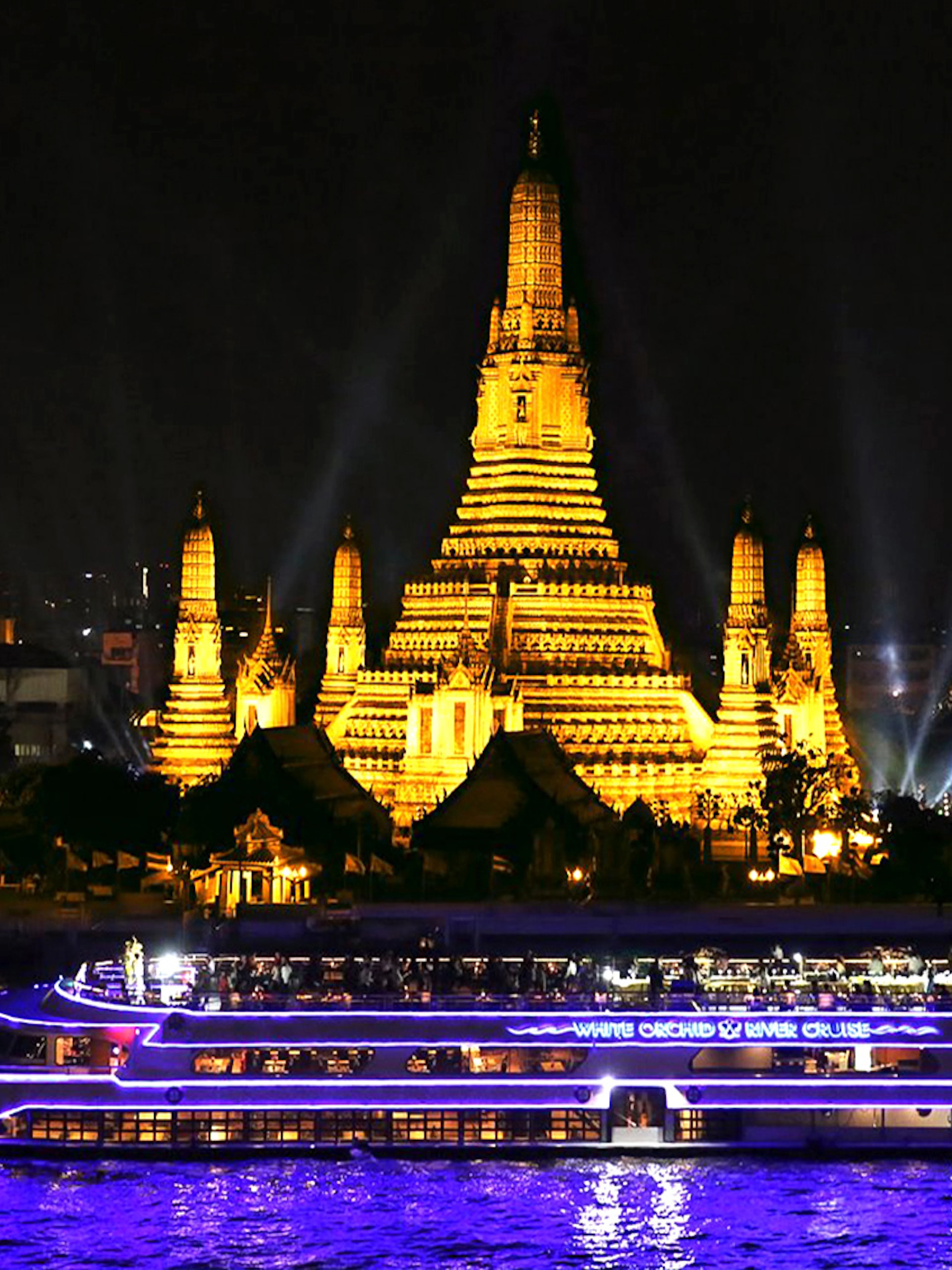 River cruise boat passing Wat Arun temple in Bangkok at night.