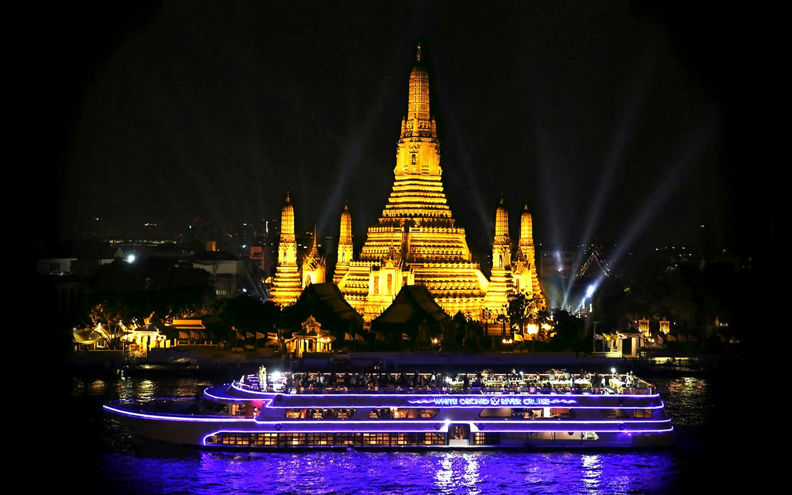 River cruise boat passing Wat Arun temple in Bangkok at night.