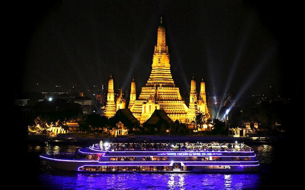 River cruise boat passing Wat Arun temple in Bangkok at night.