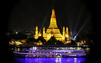 River cruise boat passing Wat Arun temple in Bangkok at night.