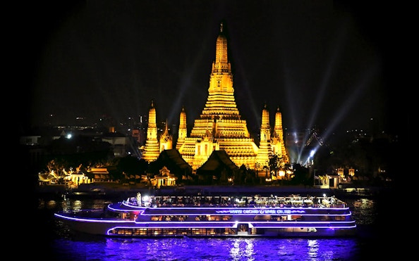 River cruise boat passing Wat Arun temple in Bangkok at night.