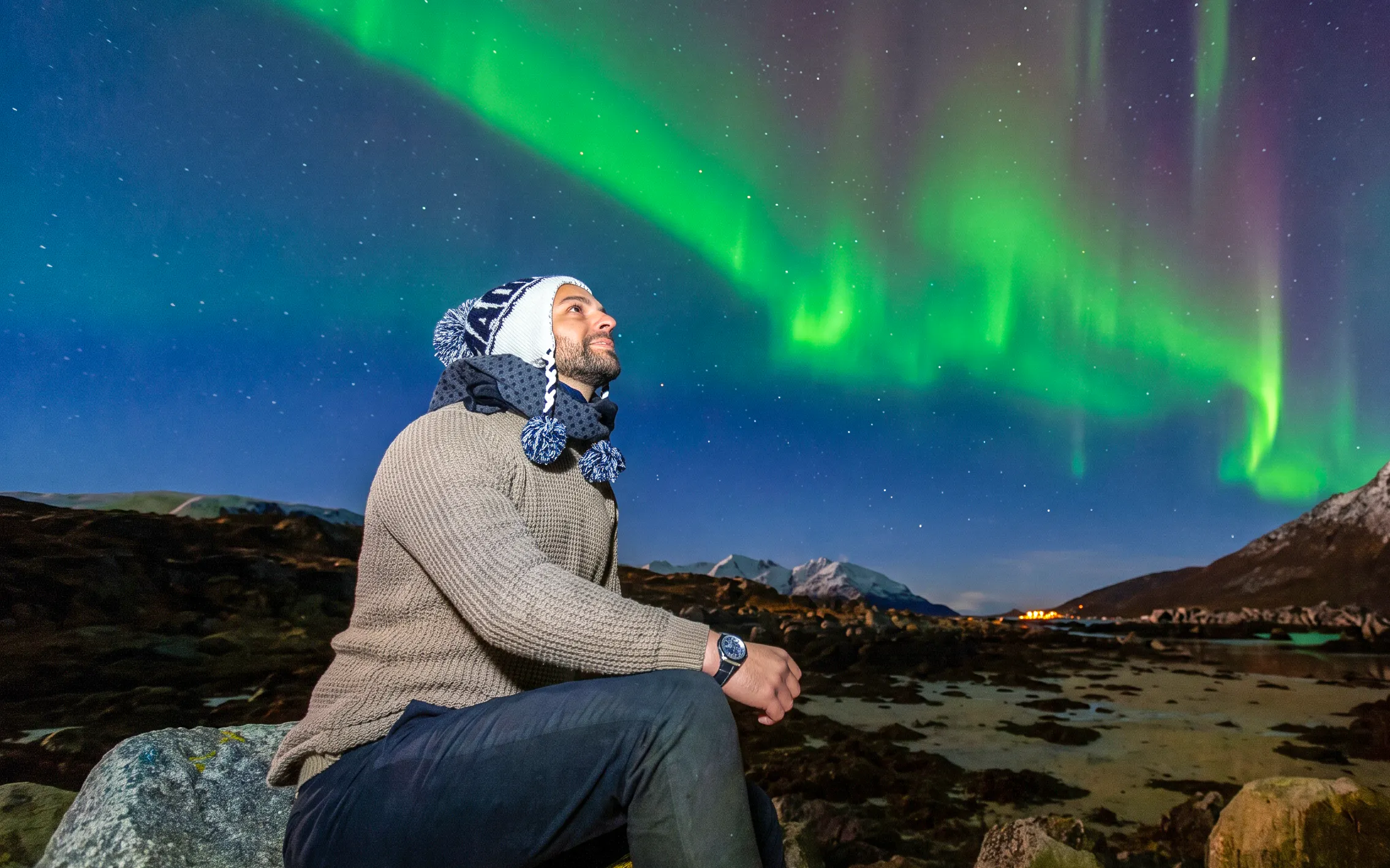 Man watching Northern Lights in Tromsø, Norway, with snowy mountains in the background.