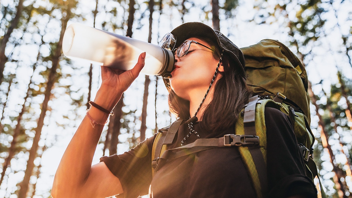 Tourist drinking water from a bottle in front of the Eiffel Tower, Paris, emphasizing hydration.