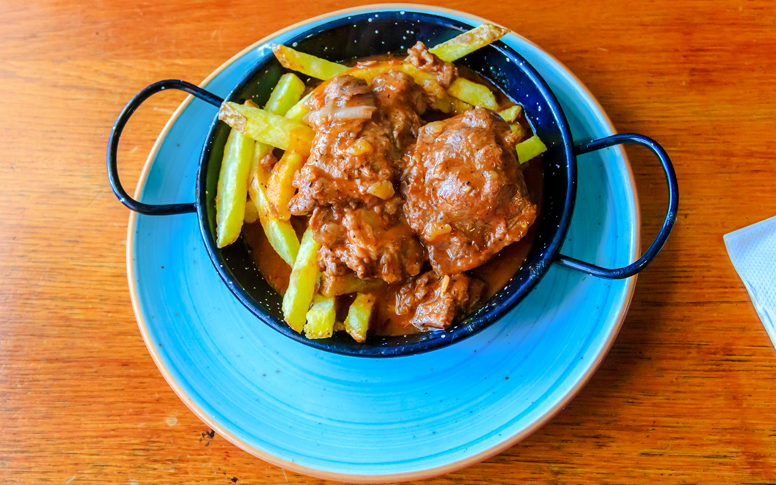 Iberian pork cheeks with fries in a black dish on a wooden table.