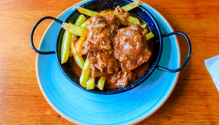 Iberian pork cheeks with fries in a black dish on a wooden table.