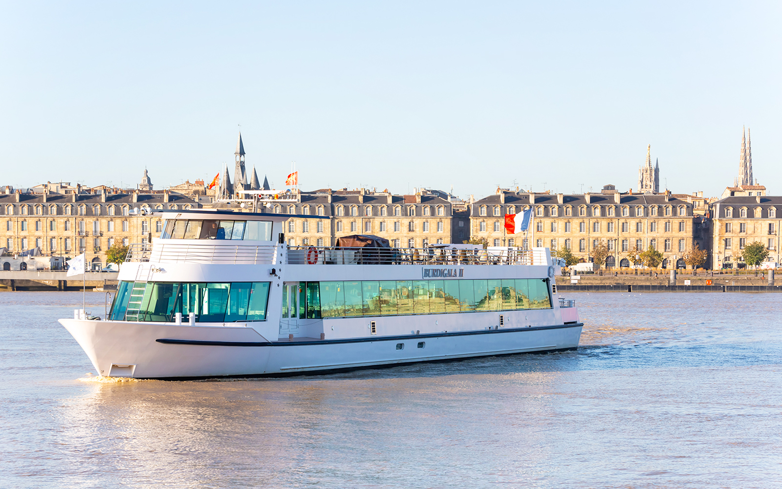 River cruise boat on the Garonne River with Bordeaux cityscape in the background.