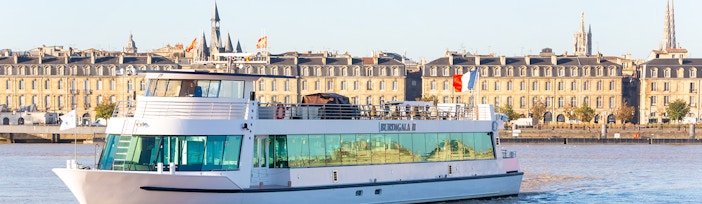 River cruise boat on the Garonne River with Bordeaux cityscape in the background.