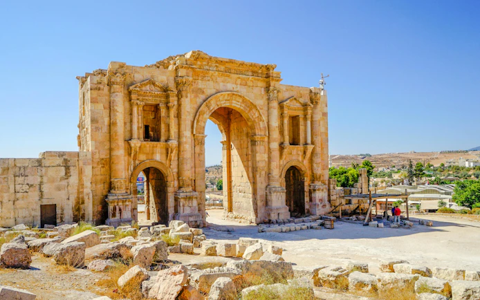 Hadrian's Arch in Jerash, Jordan, with ancient stone ruins in the foreground.