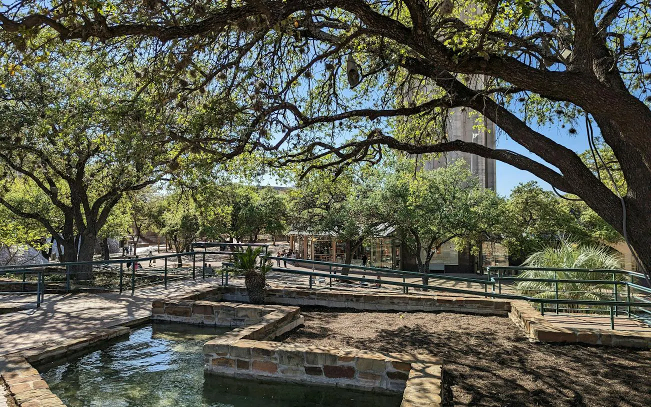 San Antonio park with trees and stone pathways, part of self-guided city exploration game.