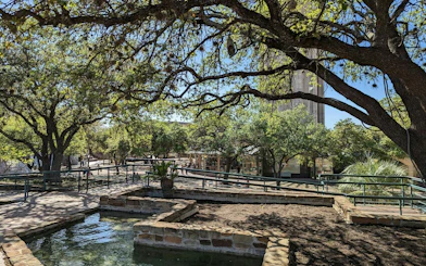 San Antonio park with trees and stone pathways, part of self-guided city exploration game.