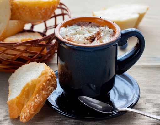Hot chocolate with whipped cream in a mug beside a basket of sliced baguette.