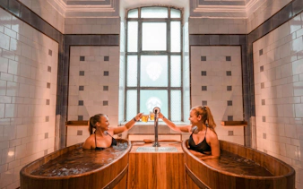 Guests toasting with beers in wooden tubs at Szechenyi Spa Beer Spa, Budapest.