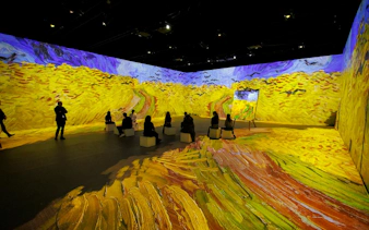 Visitors seated in Van Gogh immersive exhibit, Zurich, with vibrant wheat field projections.