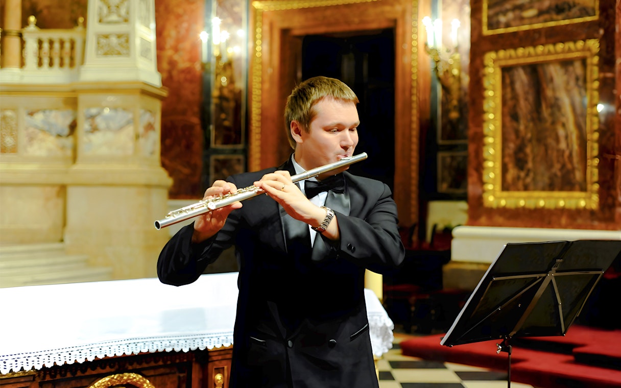 Man in black suit playing silver flute at St. Stephen's Basilica concert.