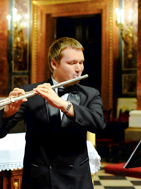 Man in black suit playing silver flute at St. Stephen's Basilica concert.