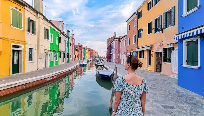 Tourist woman with hat viewing colorful houses on Burano island, Italy.