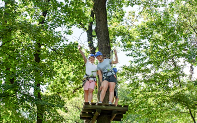 Women on zipline platform at Hanuman World Phuket surrounded by trees.