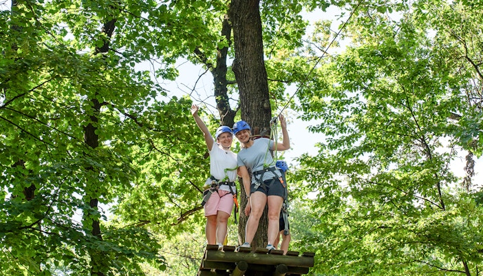 Women on zipline platform at Hanuman World Phuket surrounded by trees.