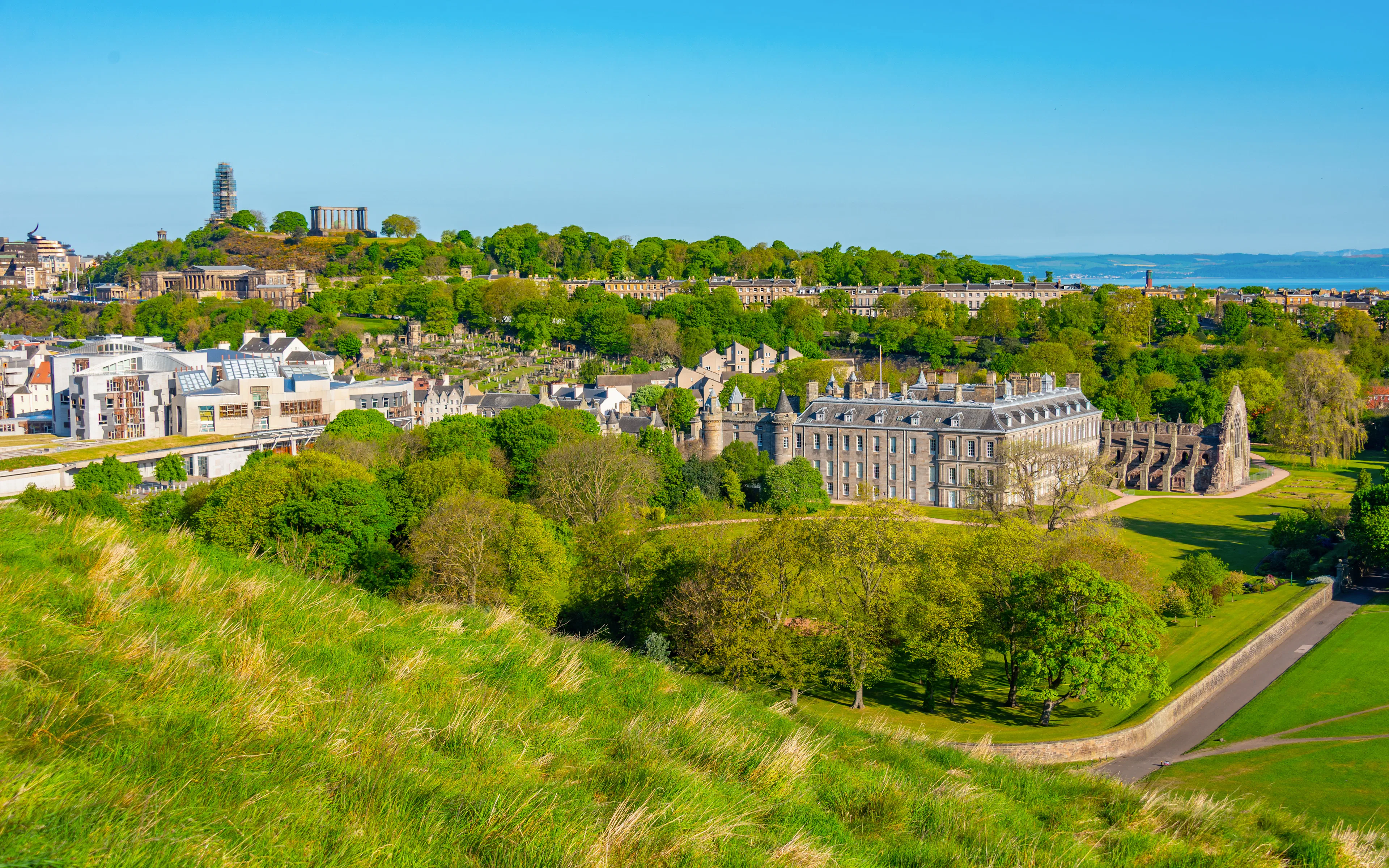 Holyroodhouse Palace and gardens in Edinburgh, surrounded by lush greenery and historic architecture.