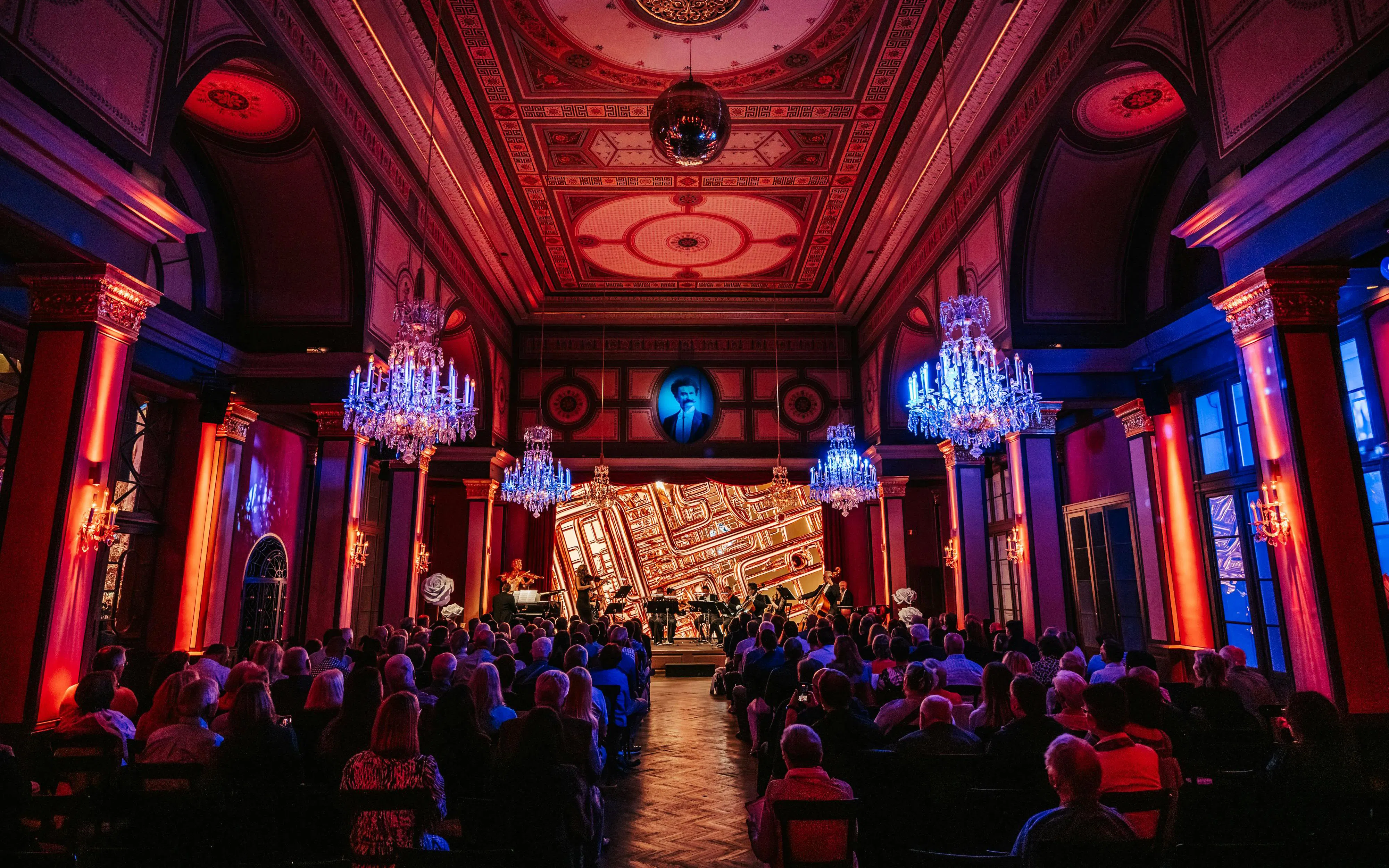 Vienna concert hall with audience and musicians performing under chandeliers.
