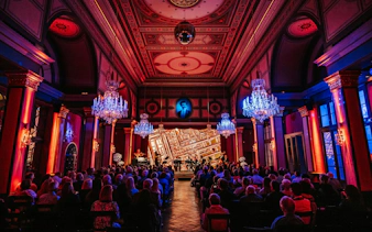 Vienna concert hall with audience and musicians performing under chandeliers.