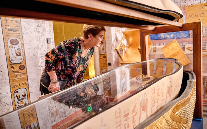 Visitor examines open sarcophagus with hieroglyphs at Tomb of the Pharaoh exhibit.