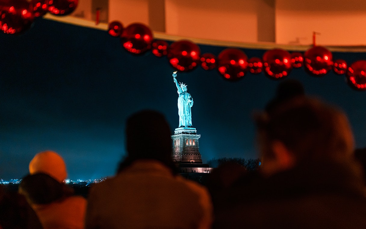 Statue of Liberty illuminated at night, viewed from a cruise with festive decorations.