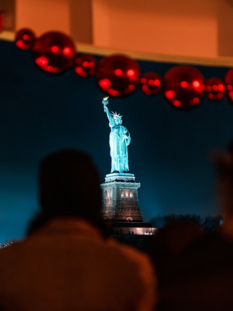 Statue of Liberty illuminated at night, viewed from a cruise with festive decorations.
