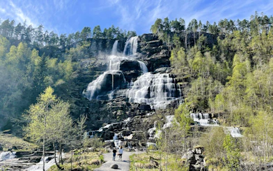 Tvindefossen Waterfall cascading over rocky cliffs with visitors walking on a path below.
