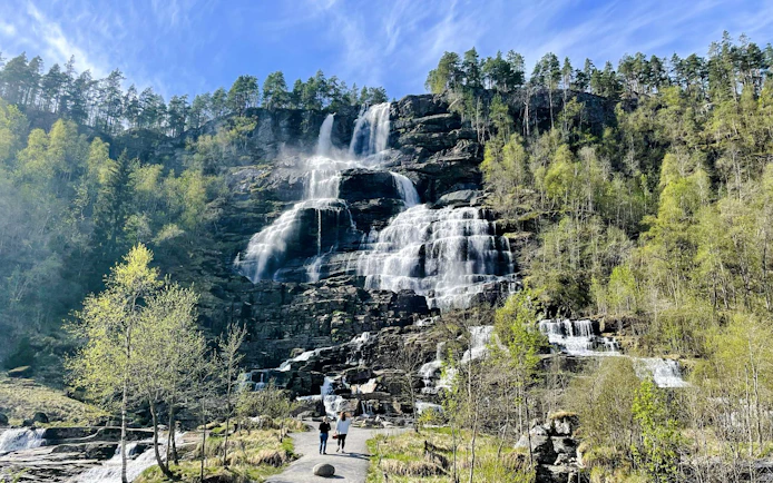 Tvindefossen Waterfall cascading over rocky cliffs with visitors walking on a path below.