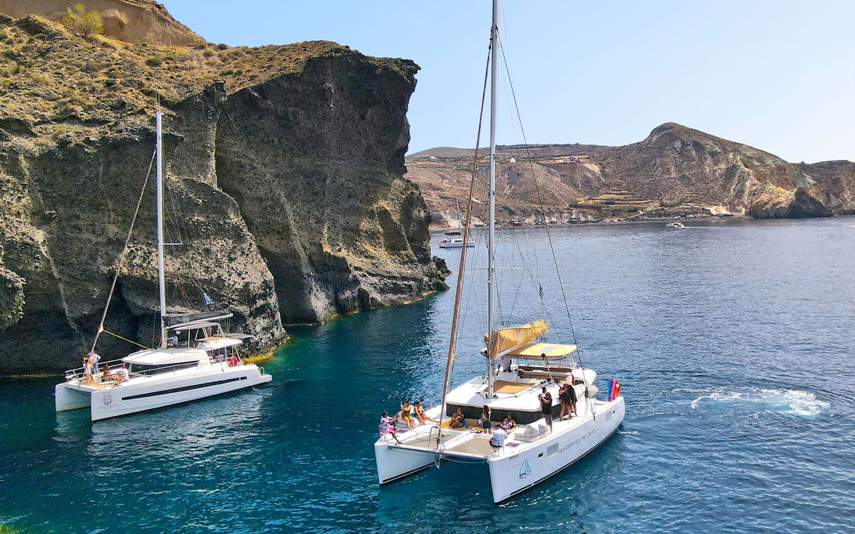 Catamarans sailing near rocky cliffs in Santorini, Greece.