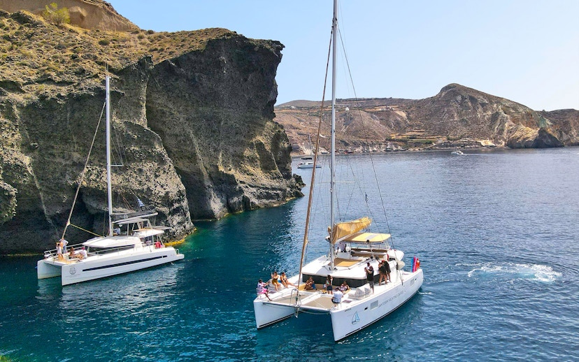 Catamarans sailing near rocky cliffs in Santorini, Greece.