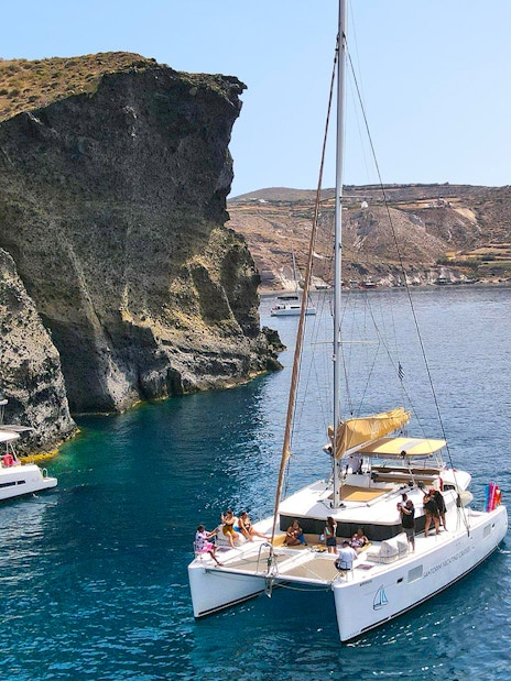 Catamarans sailing near rocky cliffs in Santorini, Greece.