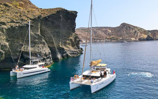 Catamarans sailing near rocky cliffs in Santorini, Greece.