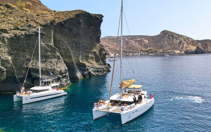 Catamarans sailing near rocky cliffs in Santorini, Greece.