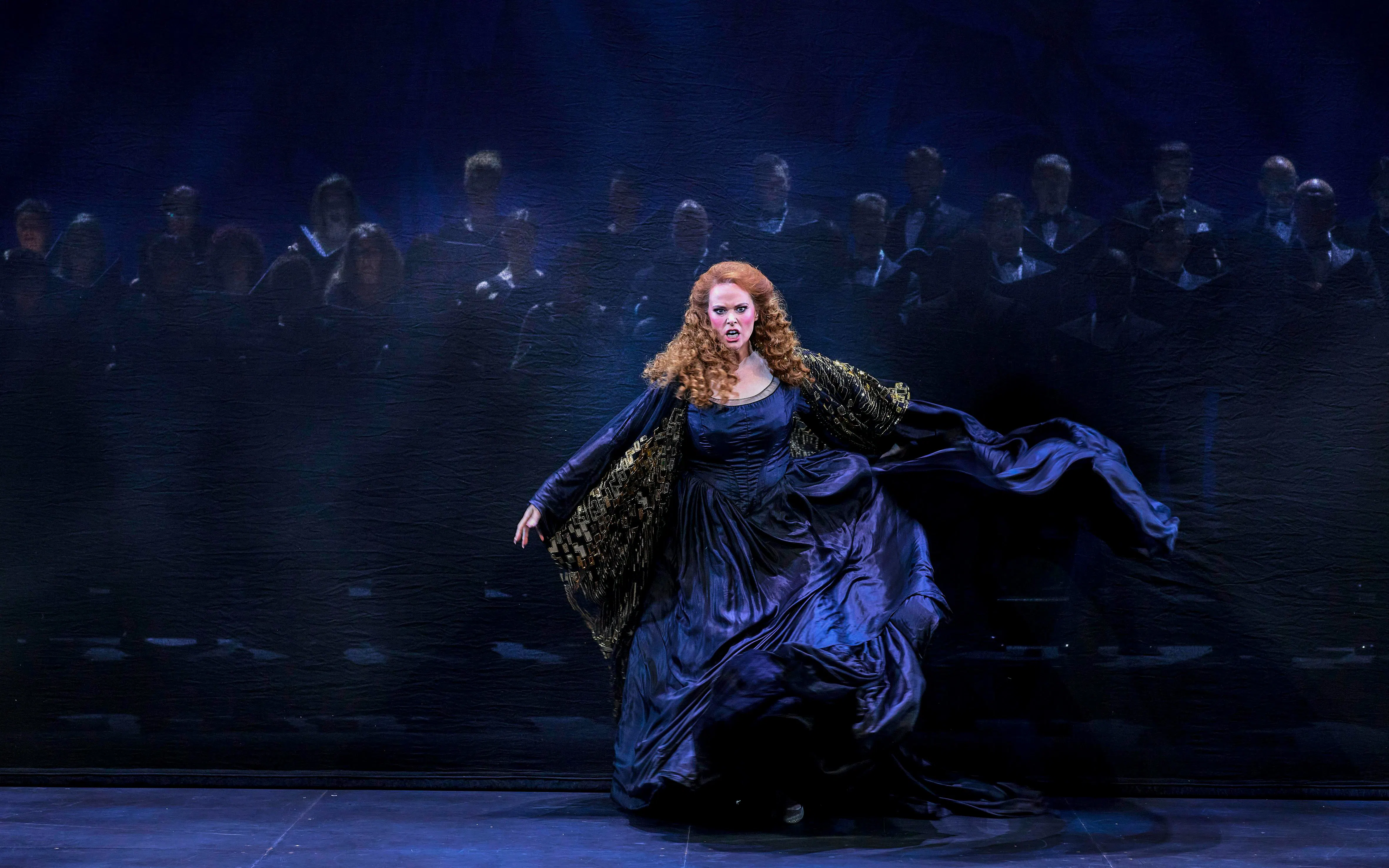 A performer in a dramatic scene from My Fair Lady, with a choir in the background.