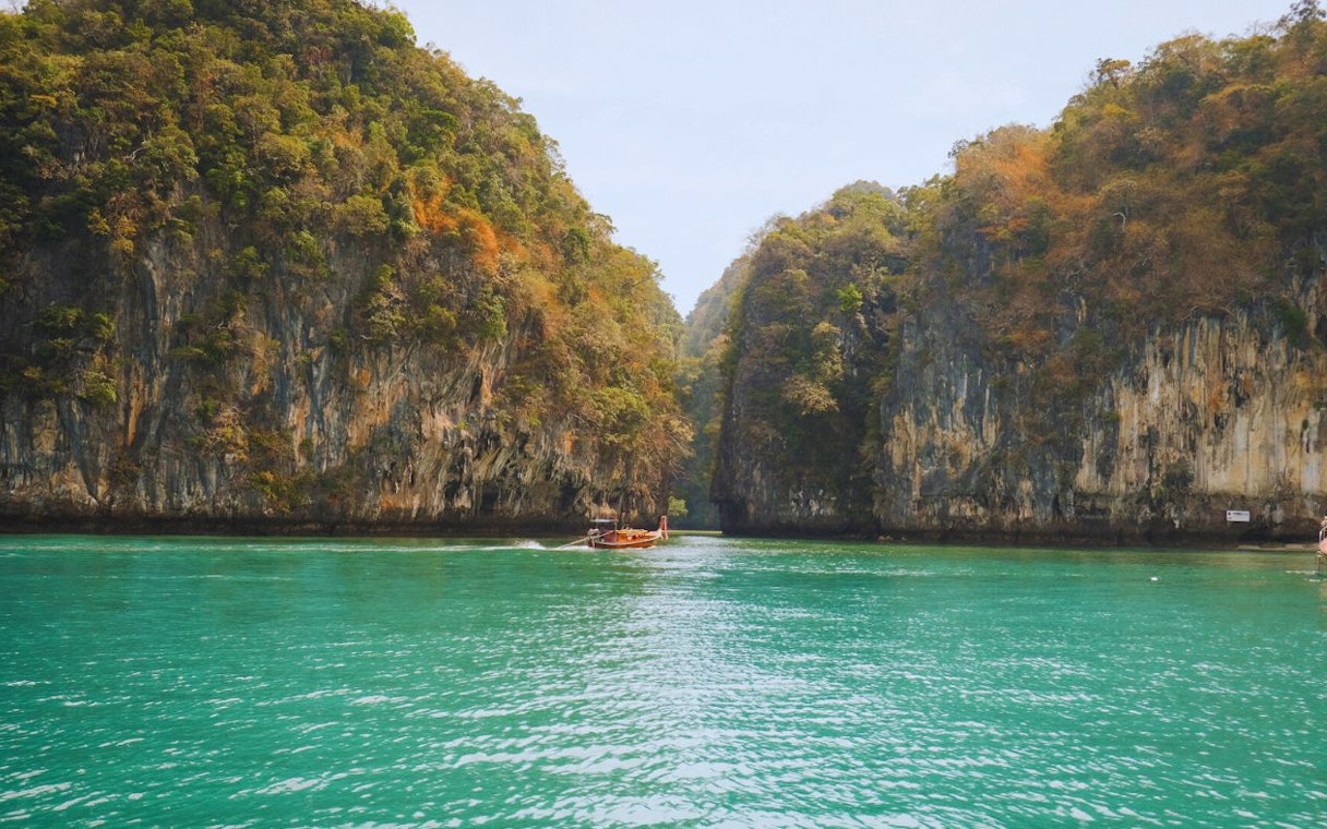 Longtail boat navigating turquoise waters between limestone cliffs at Hong Island, Krabi, Thailand.