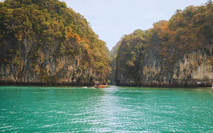 Longtail boat navigating turquoise waters between limestone cliffs at Hong Island, Krabi, Thailand.