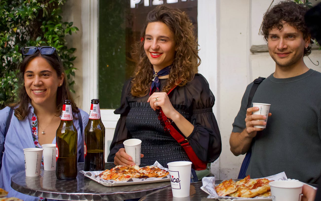 Visitors enjoying pizza and drinks during a food tour in Trastevere, Rome.
