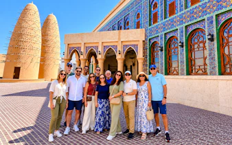 Group of tourists at Katara Cultural Village, Doha, with traditional architecture and pigeon towers.